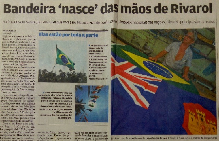 Recorte do jornal A Tribuna com a manchete “Bandeira ‘nasce’ das mãos de Rivarol” e a foto do Seu Riva na mesa de corte, com as bandeiras